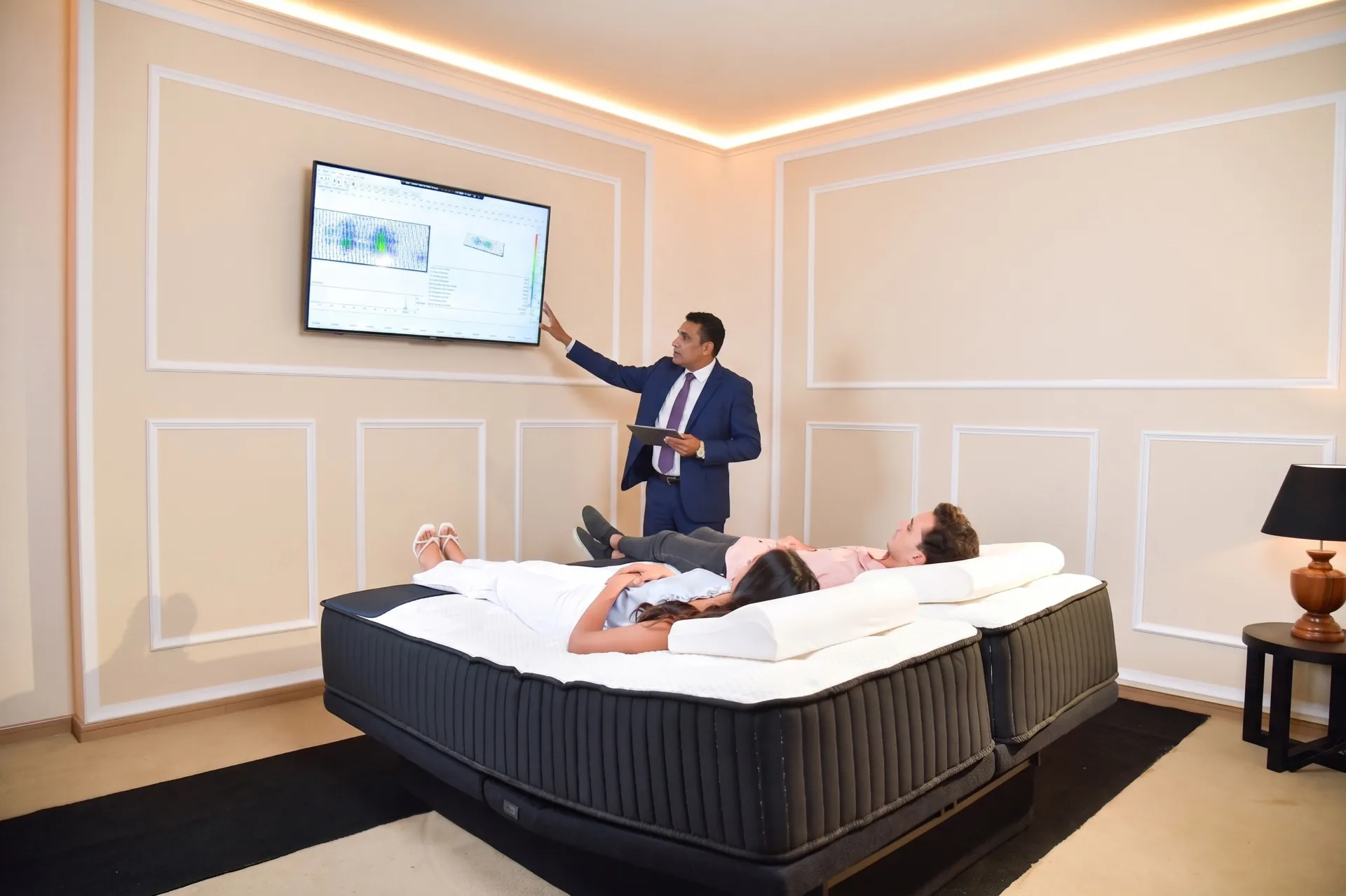 A sleep consultant explaining a pressure map to two customers lying on a mattress at the Sleep Technology Centre.